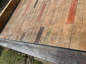 Close-up of wood-plank stamped concrete showing varied Crimson, Cumin, and Aztec Brown plank colors beside a glossy charcoal border