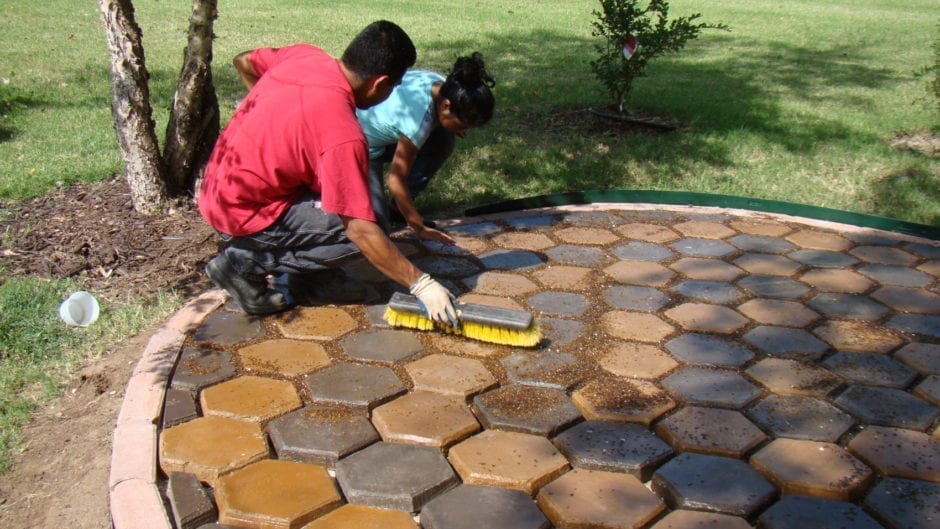 Workers applying finishing touches to stained hexagonal concrete pavers in a garden