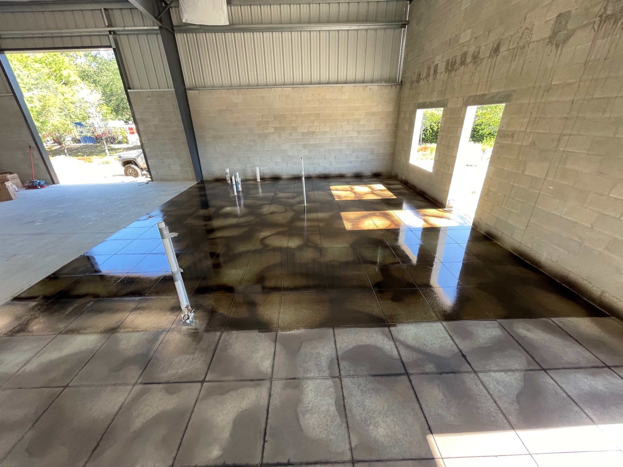 Photo of a concrete floor showcasing 3/4 of its surface, with the first coat of sealer applied, revealing vibrant, popping colors compared to the unsealed chalky light area.