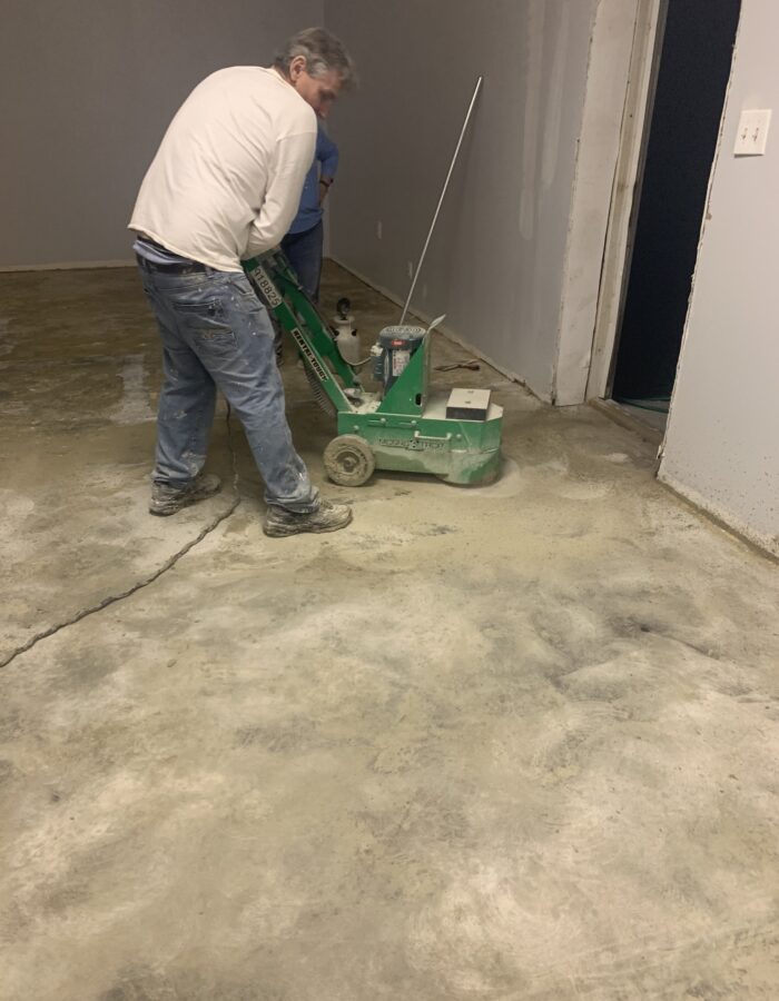 Man using a concrete grinder to remove stubborn carpet glue from a concrete floor