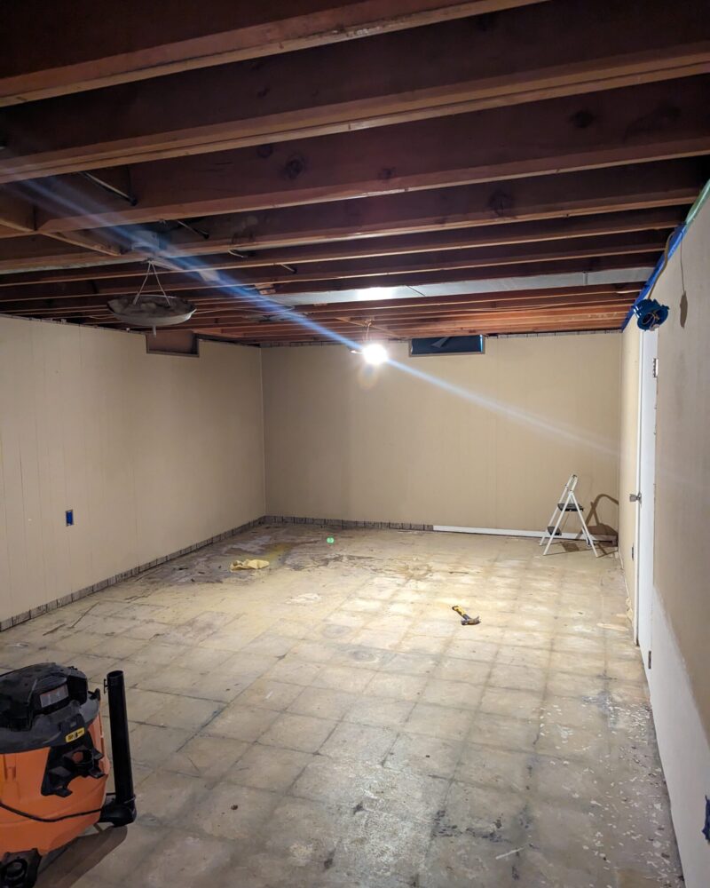 Image of a basement floor covered in mastic, showing the ghosting of tiles once under the carpet