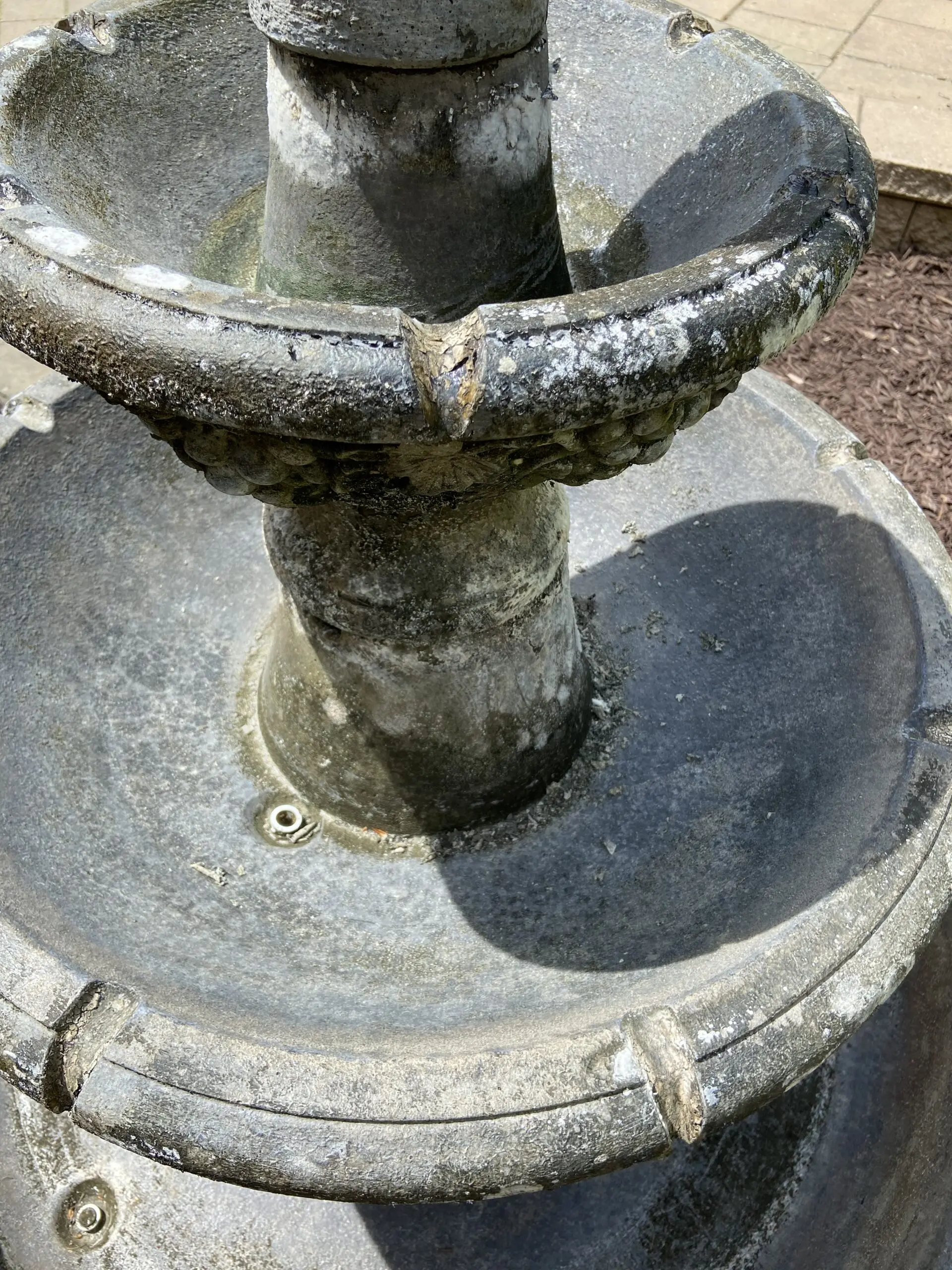 A weathered, three-tier fountain in desperate need of restoration. The impact of harsh Ohio winters and sun fading is evident on the faded concrete structure