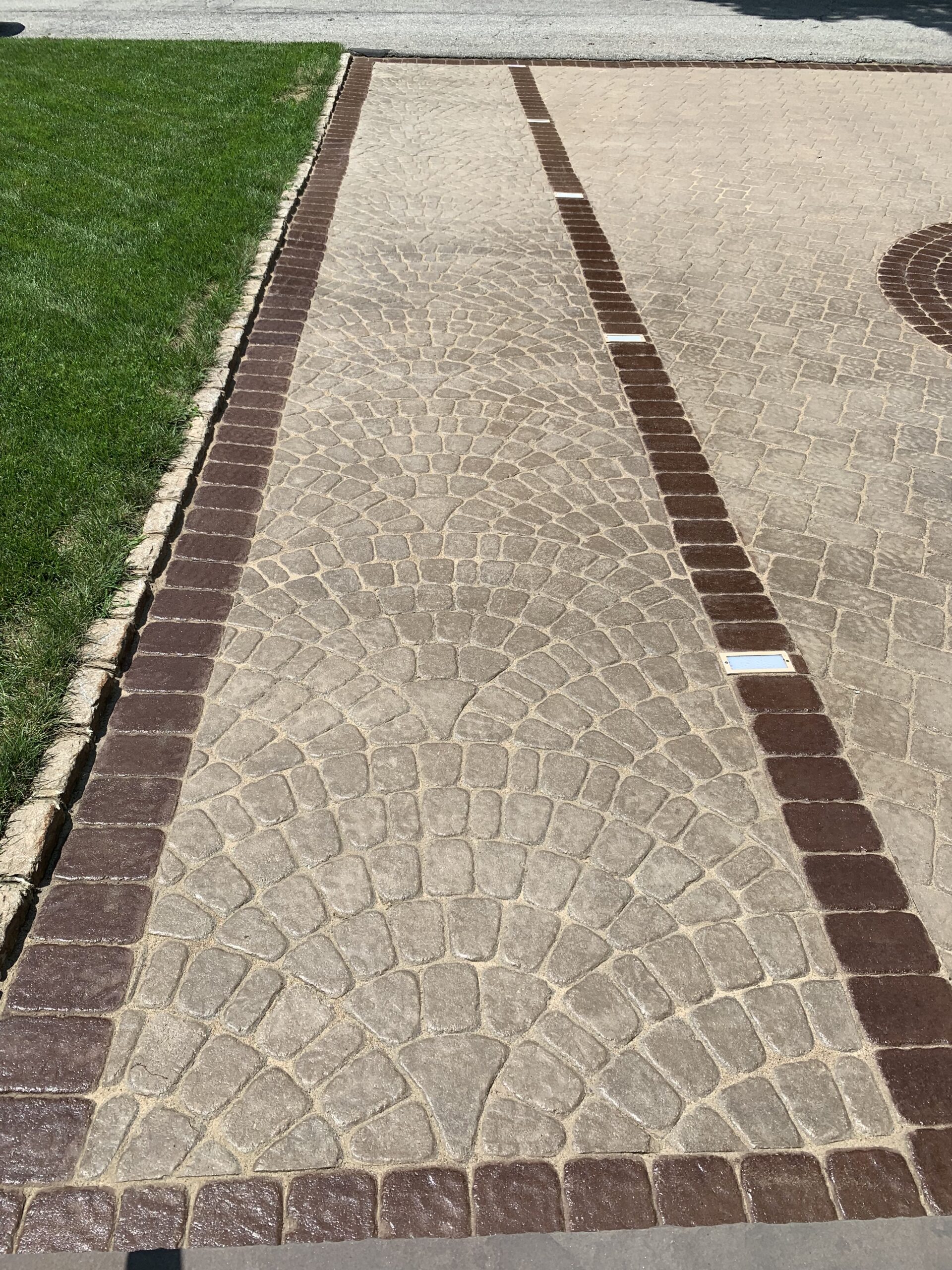 Portico Stain accent detail frame of a paver driveway using Aztec Brown. The stain has been applied to create a contrasting border around the driveway, framing the main surface area in a sleek and modern design.