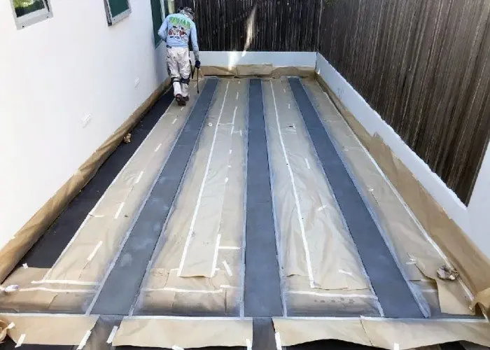 This image shows the next step in the concrete driveway staining process, where the previously stained areas with Stormy Gray Vibrance Dye are now covered and the uncovered areas are being stained with Light Slate Vibrance Dye.