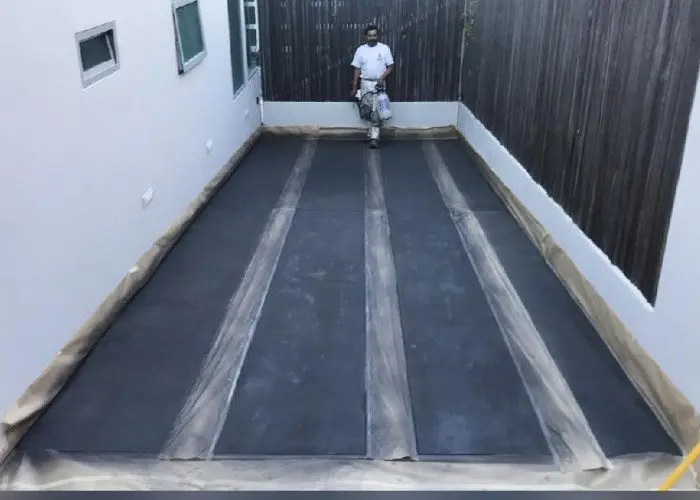 This image showcases a concrete driveway with a stunning geometric design, achieved through the application of Stormy Gray Vibrance Dye. The process involved carefully avoiding the areas that were taped off to remain a lighter color, resulting in a unique and eye-catching design.