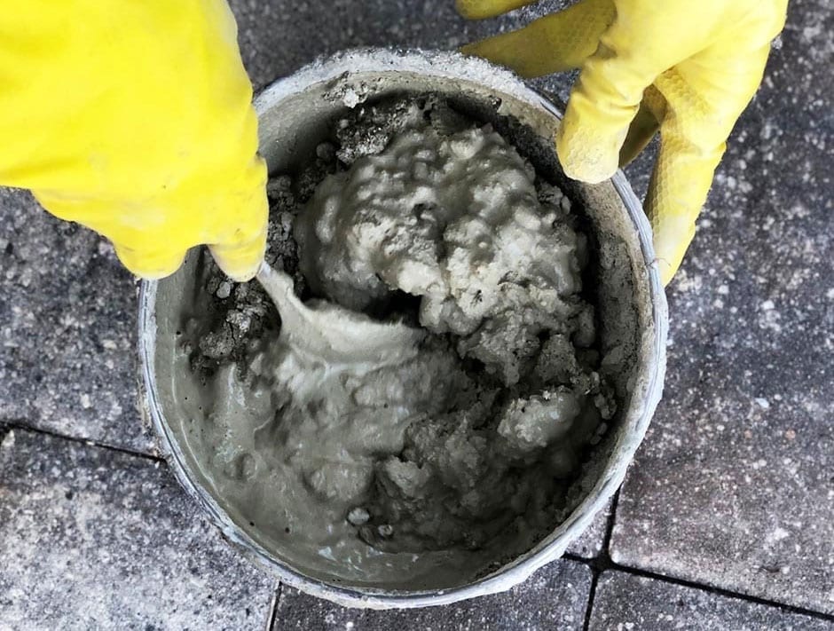 Person mixing dry cement and water in a large bucket to create a smooth concrete mixture for a DIY project