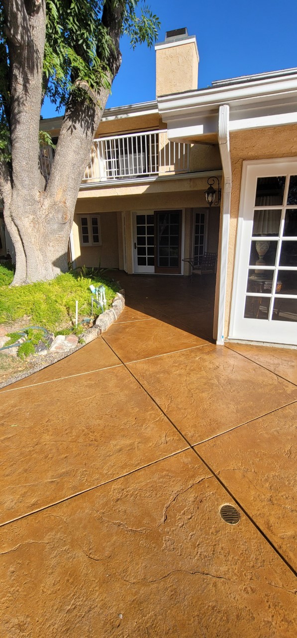 An after photo showing the refreshed stamped concrete around the pool, fire pit, and other areas of the backyard, now stained with a rich Yukon Gold color and sealed with a satin finish