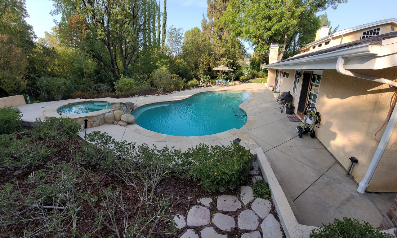 A before photo showing a wide expanse of faded and colorless stamped concrete around a pool, fire pit, and extending to other areas of the backyard