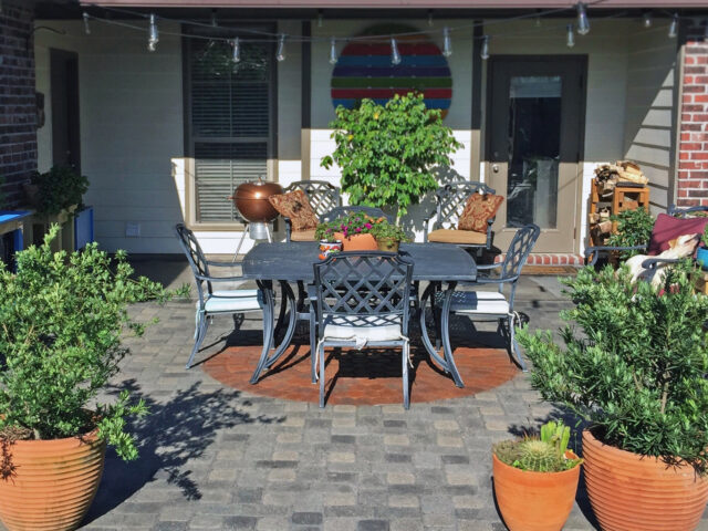 A circular paver design in warm terracotta hues is surrounded by charcoal Portico stained patio concrete pavers.