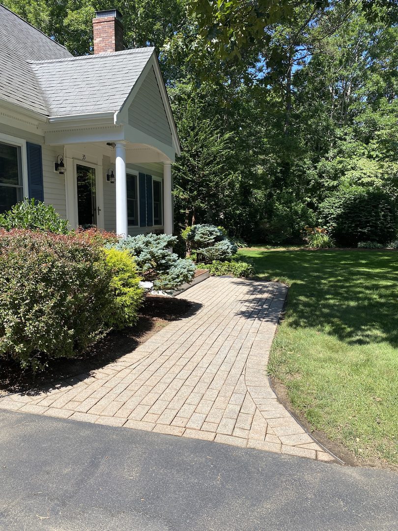 A plain, faded paver walkway leading to a cozy home entrance