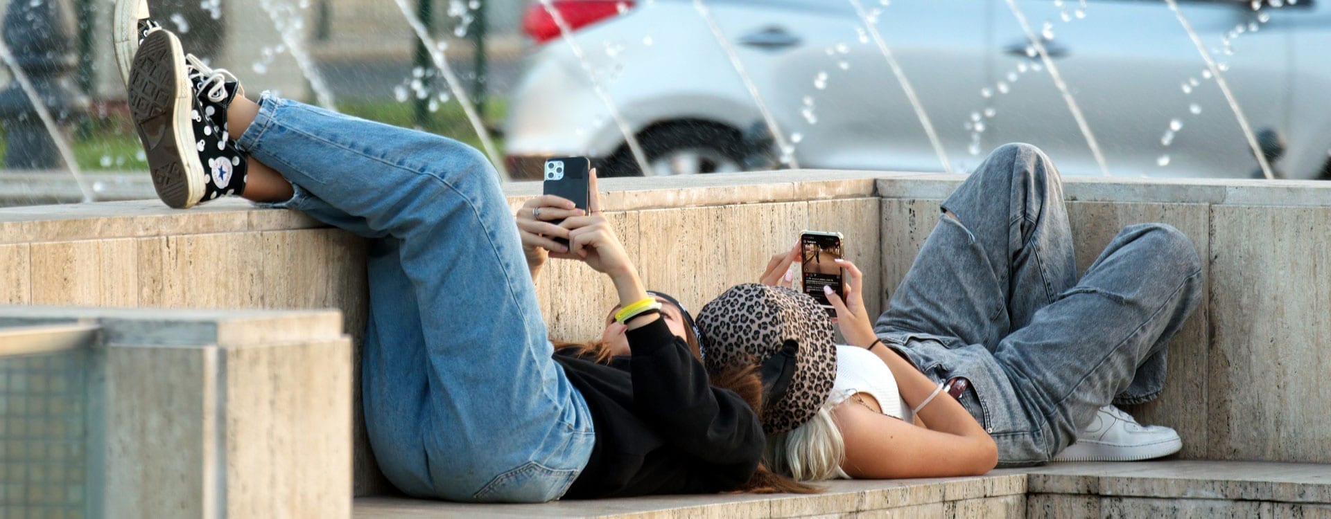 Two women lounge on a concrete bench looking up the answer to what is concrete.