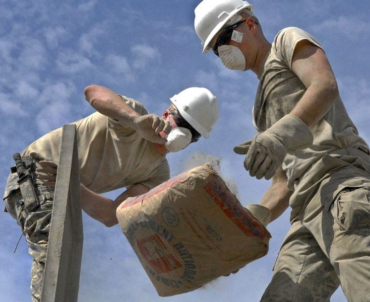 Two construction workers handle bags of ready-mix concrete at a job site.