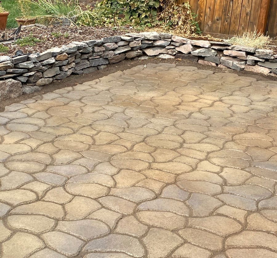 A backyard concrete pavers patio is stained with olive and charcoal concrete acid stains.