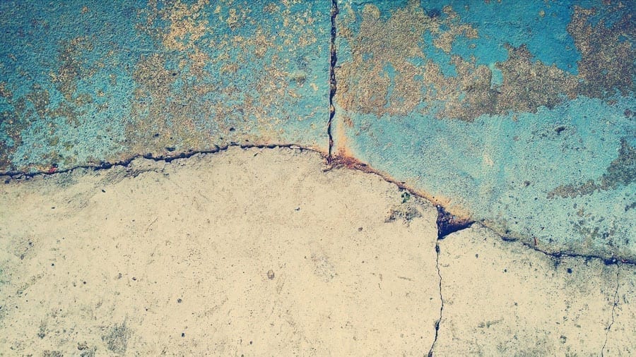 A grey and blue concrete slab cracked and rusted.