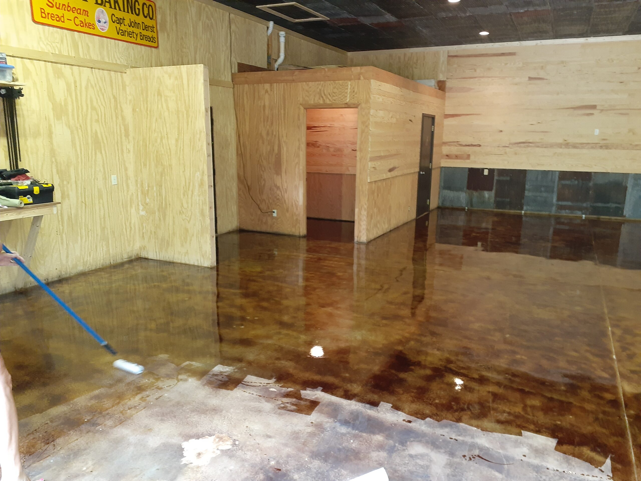 Roller applying high gloss EasySeal sealer on coffee brown acid stain concrete garage floor