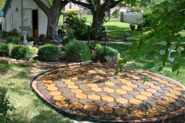 Completed circular patio with Driftwood and Yukon Gold stained hexagonal pavers surrounded by lush landscaping.