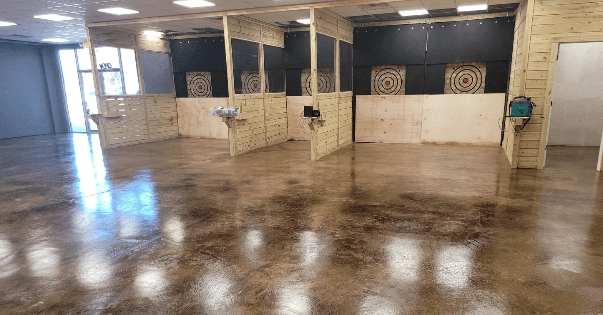 commercial concrete floor featuring a coffee brown acid stain, creating a rich and warm leather-like finish, complemented by wooden accents and target boards on the walls.