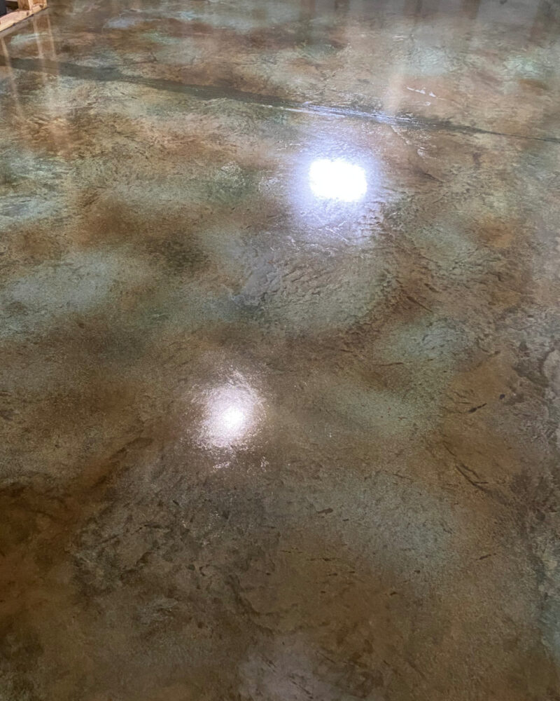 A photo of a concrete floor with the first coat of sealer applied, showing a glossy surface