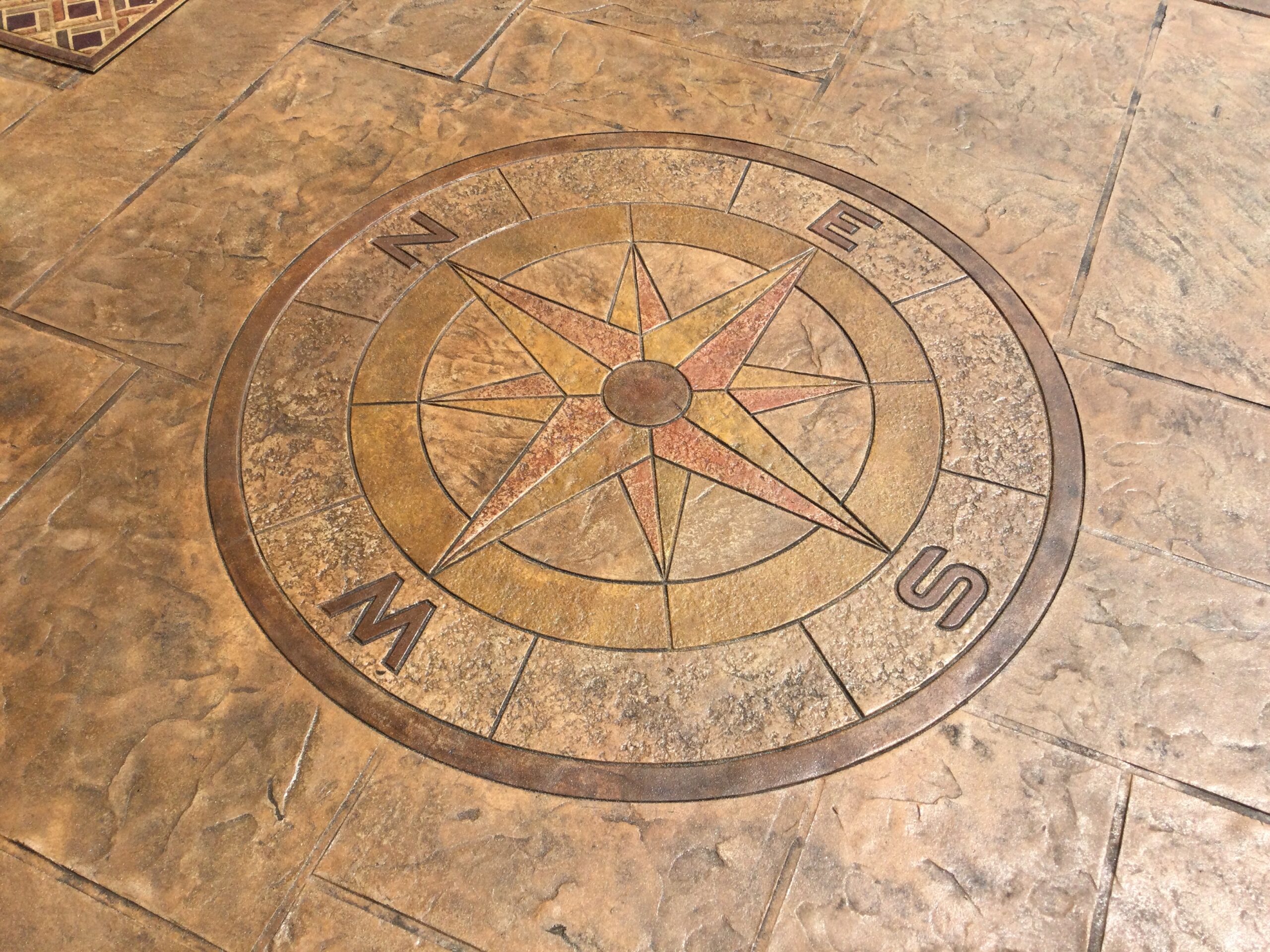 Stamped concrete compass design in warm tones, featuring Wheat, Black, Cafe Royale, Crimson, and Driftwood colors.