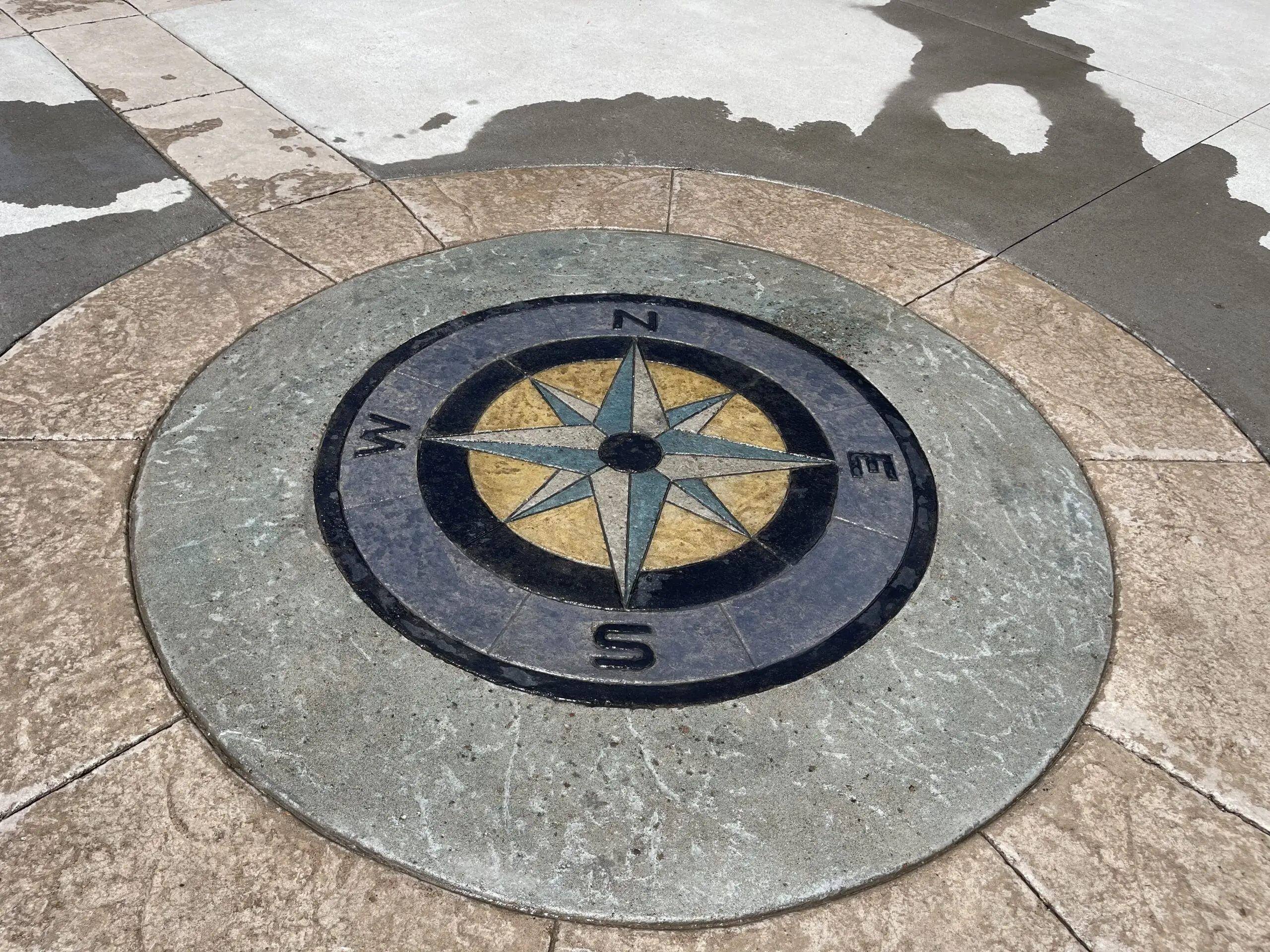 A decorative concrete compass stained in ColorWave Black, Iron Gray, Navy, and Yellow, with intricate detail and a weathered look