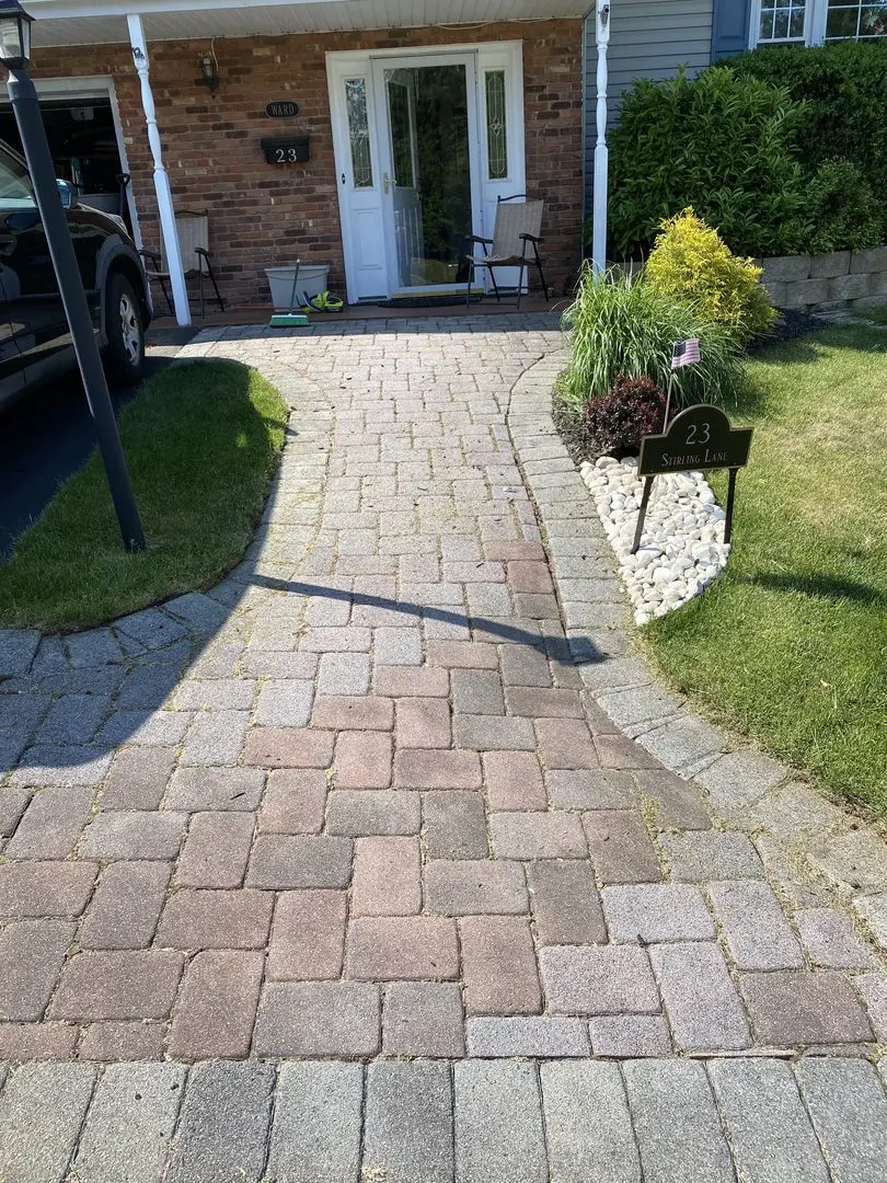 A walkway with unevenly discolored pavers leading to a home's entrance, before restoration