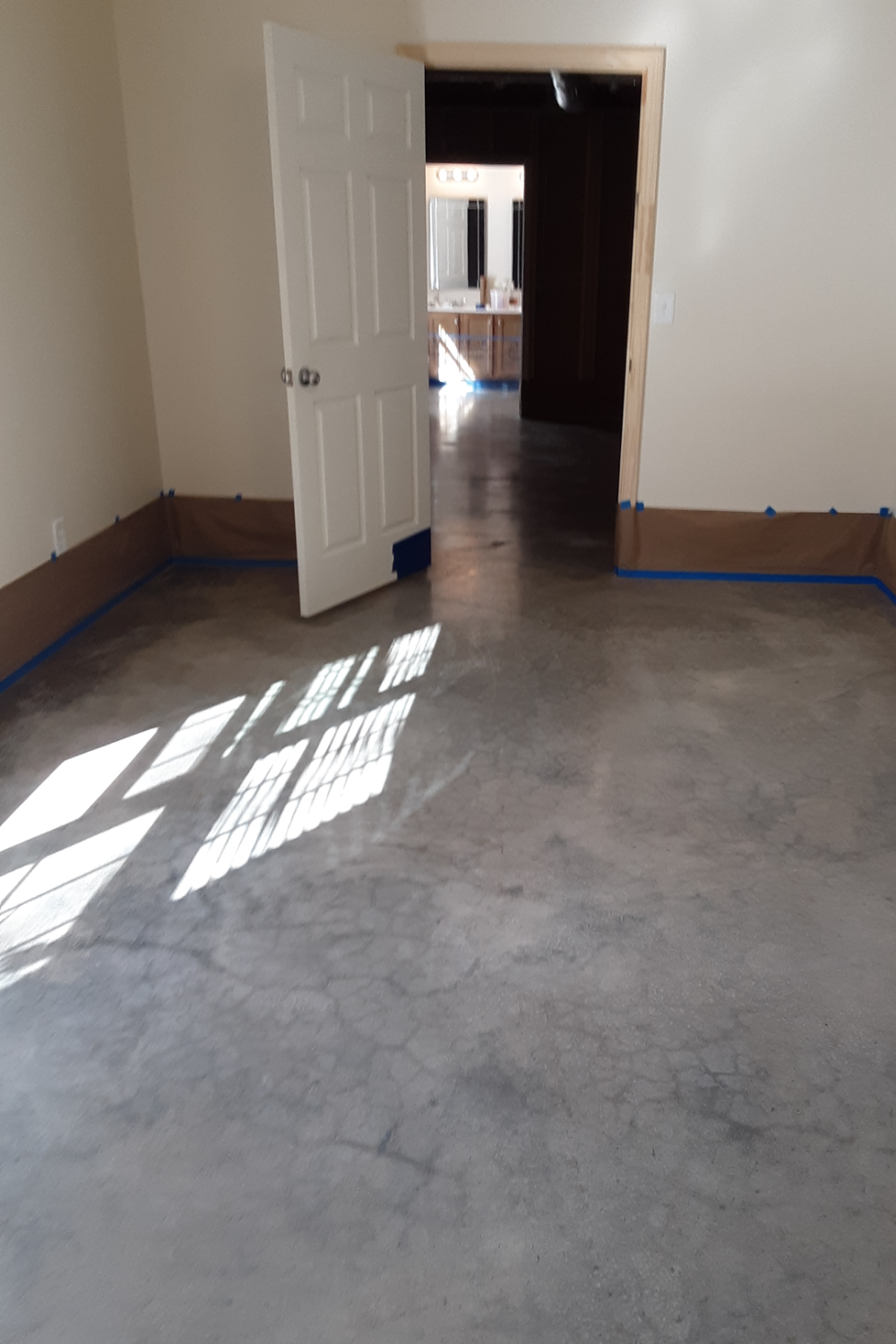 An unfinished basement with a raw concrete floor, taped-off walls, and natural light streaming in through a window