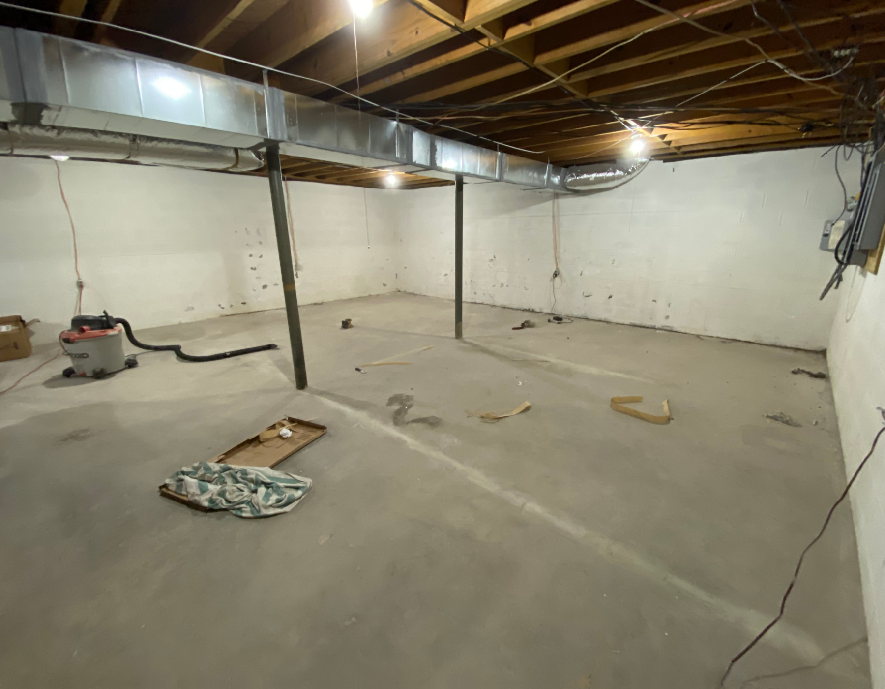 Unfinished basement space before transformation, showing bare concrete floors and exposed utilities.