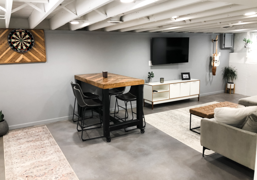 A modern basement with a Vibrance-dyed concrete floor in Charcoal, White, and Stormy Gray, featuring a lounge area and dartboard.