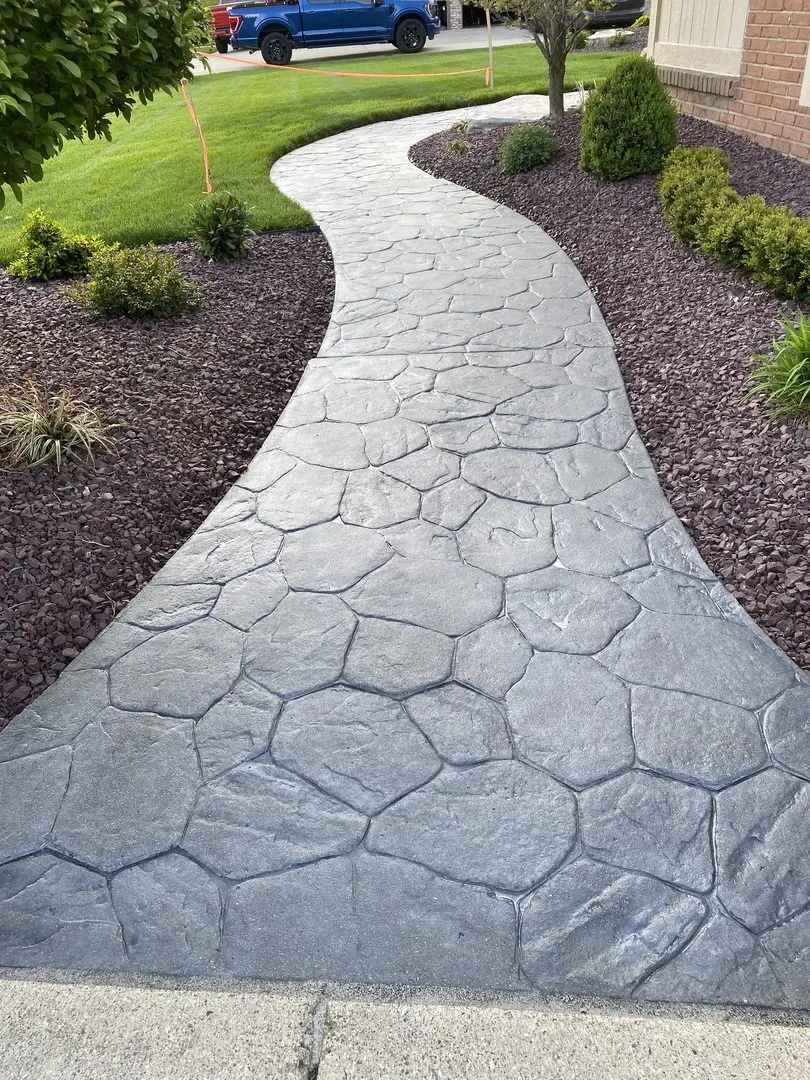 stamped concrete walkway in varying shades of gray stretches beside a manicured lawn