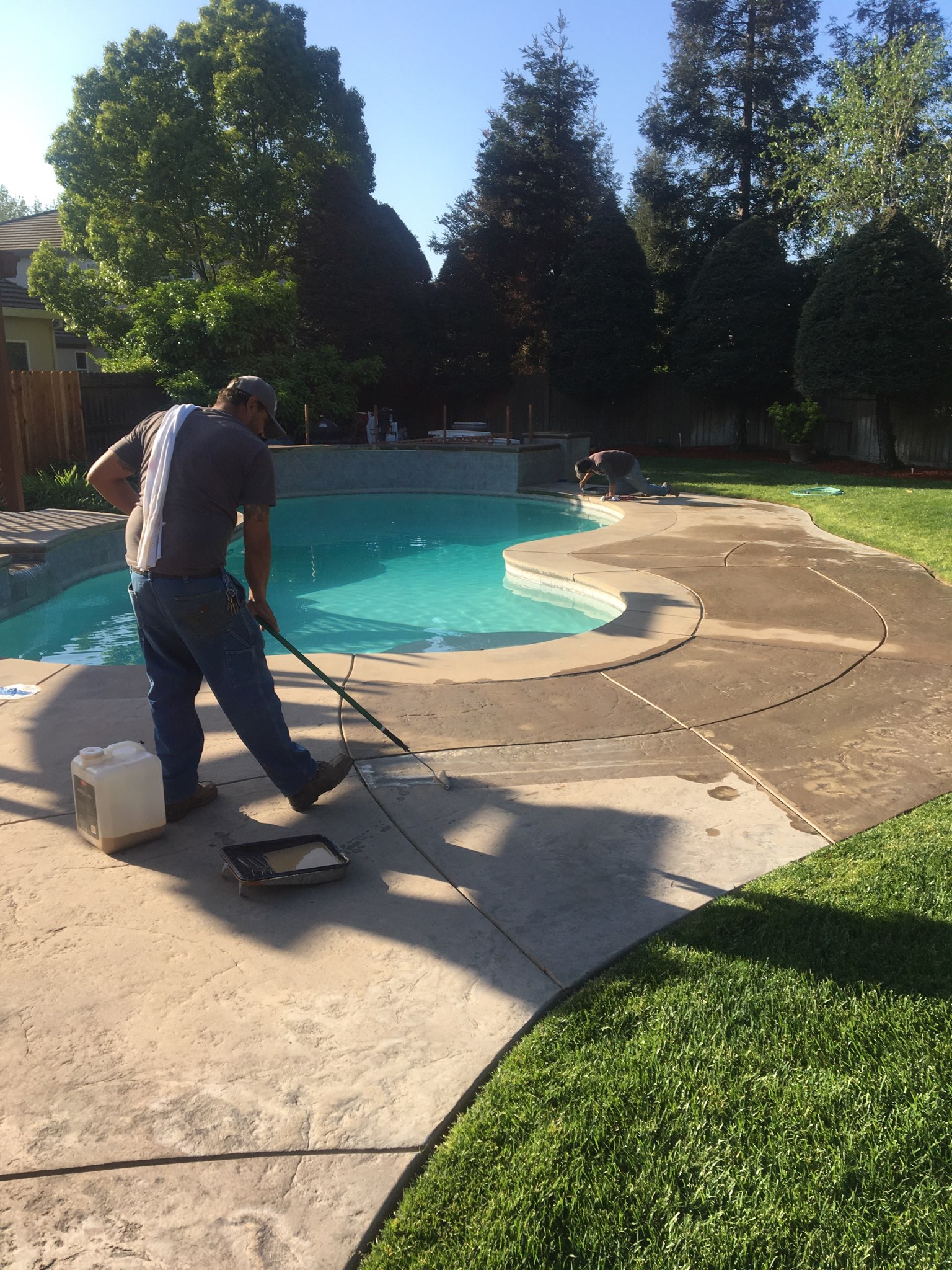 A DIYer using a roller to apply the Khaki Antiquing stain on the faded stamped concrete spa surround