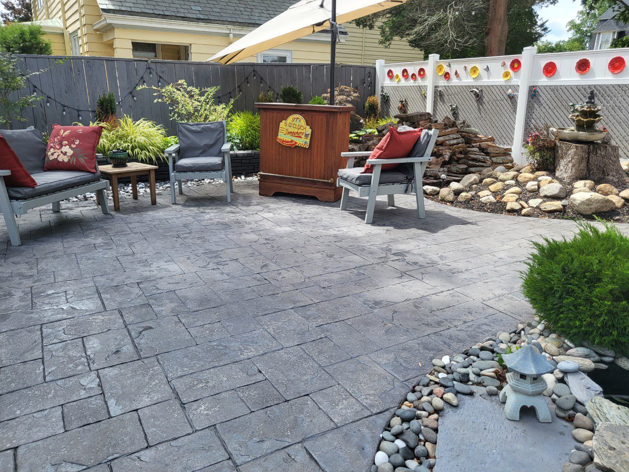 Stamped concrete patio, beautifully enhanced with a gray concrete stain and sealed for durability, showcasing intricate patterns and the sophisticated hues of the stain