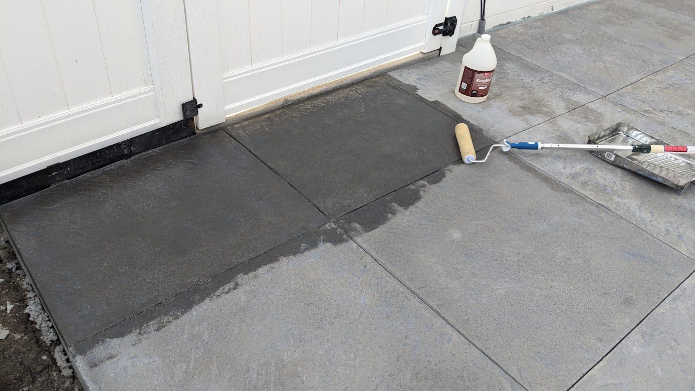Image depicting the process of sealing the freshly stained patio squares using a roller, a crucial step in enhancing the gray concrete stain's longevity and vibrancy