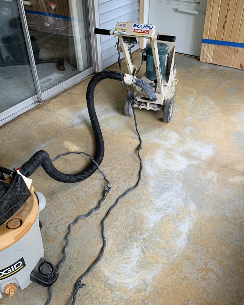 Rented grinder being used to remove carpet glue from concrete floor in preparation for acid staining