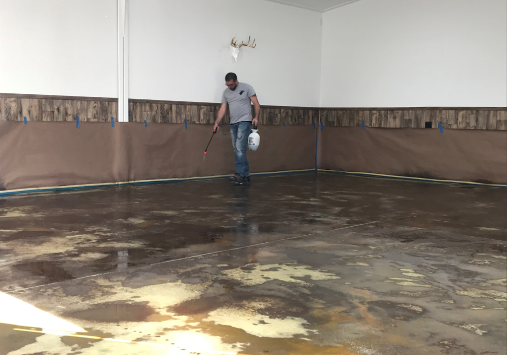 A man applying EverStain™ acid stain to a concrete floor using a pump sprayer in a garage conversion project