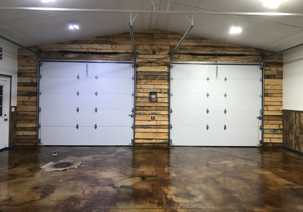 A converted garage man cave with stained concrete flooring, rustic wood walls, and large garage doors