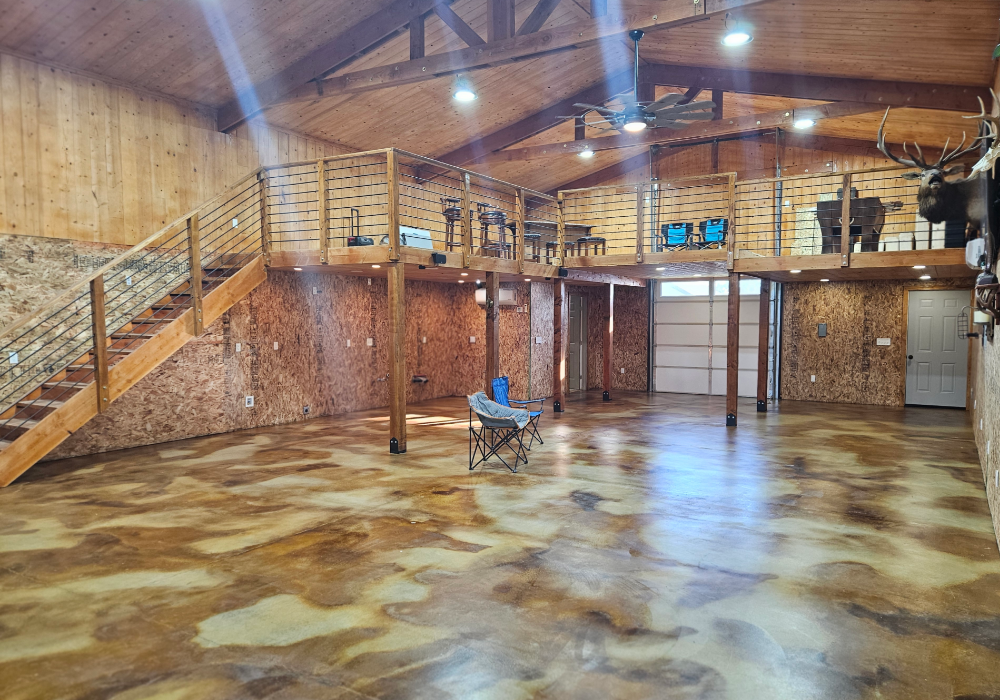 A spacious man cave with a loft, featuring a glossy acid-stained concrete floor in Coffee Brown, Cola, and Desert Amber tones.