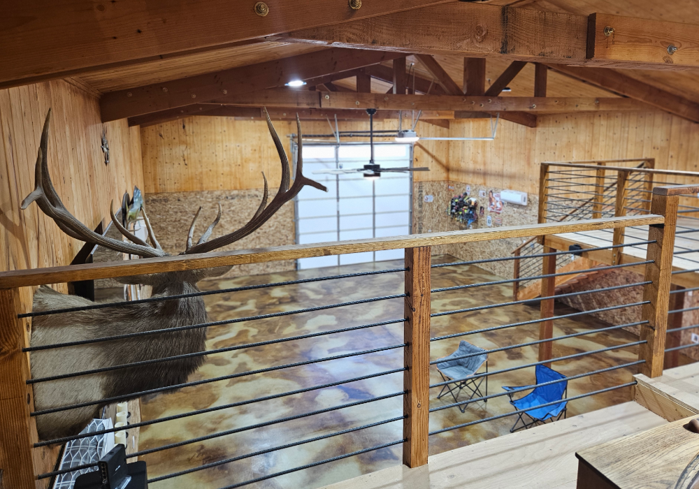 A wide-angle view of a man cave with a loft, wooden walls, and a marbled acid-stained concrete floor in earthy brown hues.