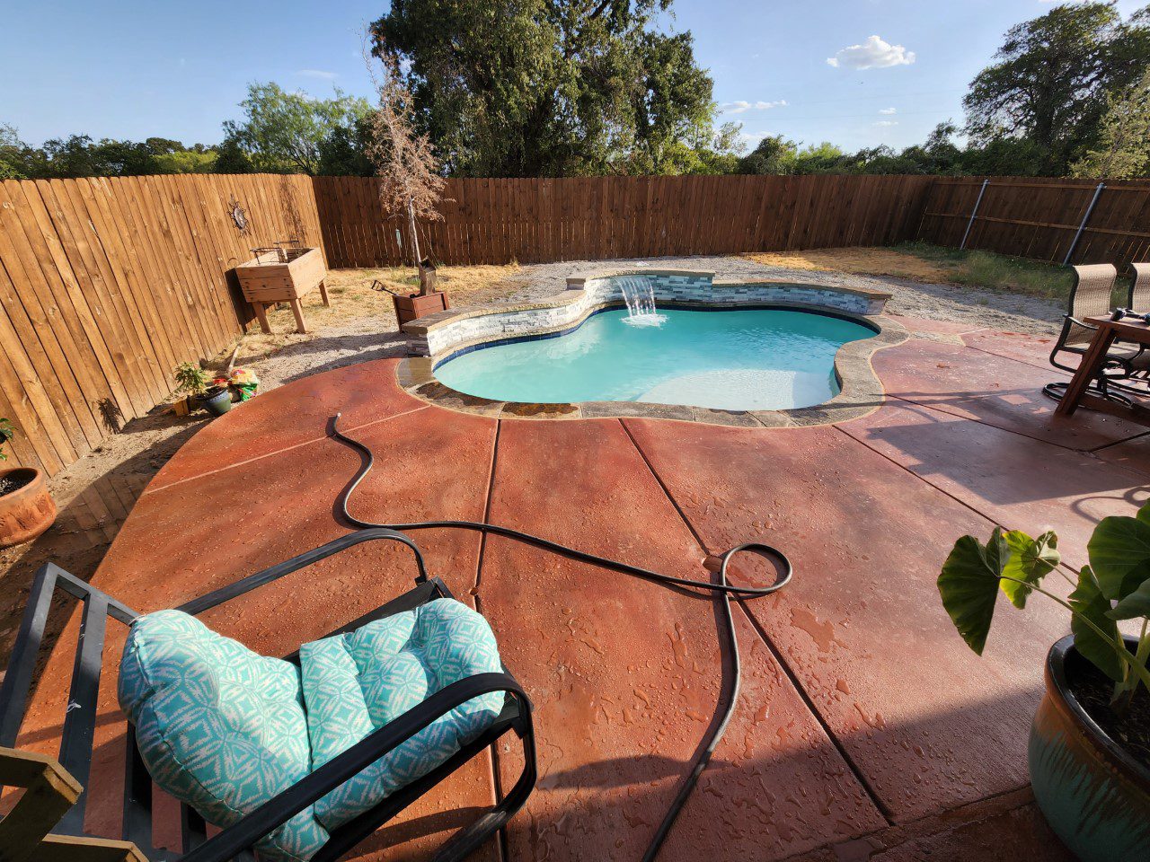 A cured newly poured concrete pool deck with a broomed finish, stained in a warm Terracotta-based hue with mottled designs highlighted in Driftwood Antiquing Stain.