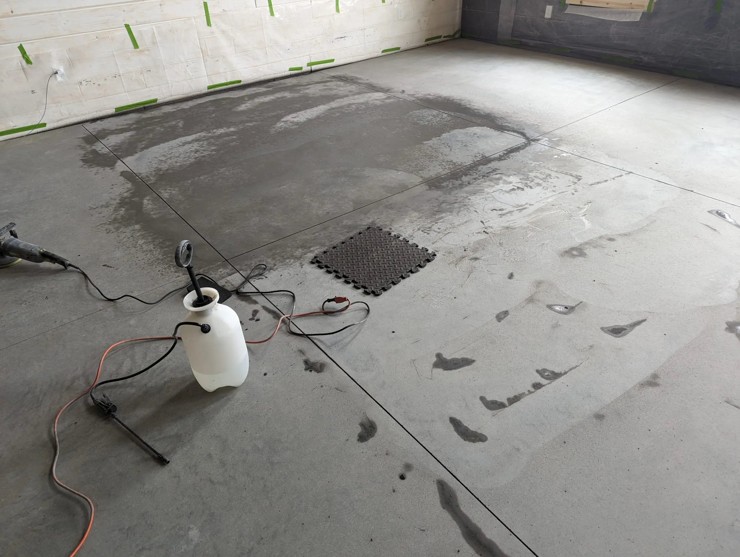 An image displaying the tools used for wet-etching the concrete floor, including a grill brick and an orbital sander, resulting in a darker and more even floor color.