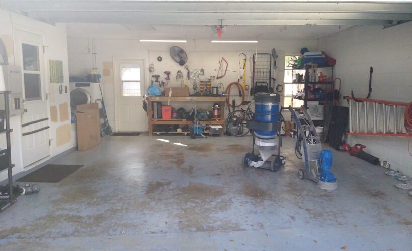 Unappealing garage with peeling coating and sealant on the floor, left behind by the previous owner