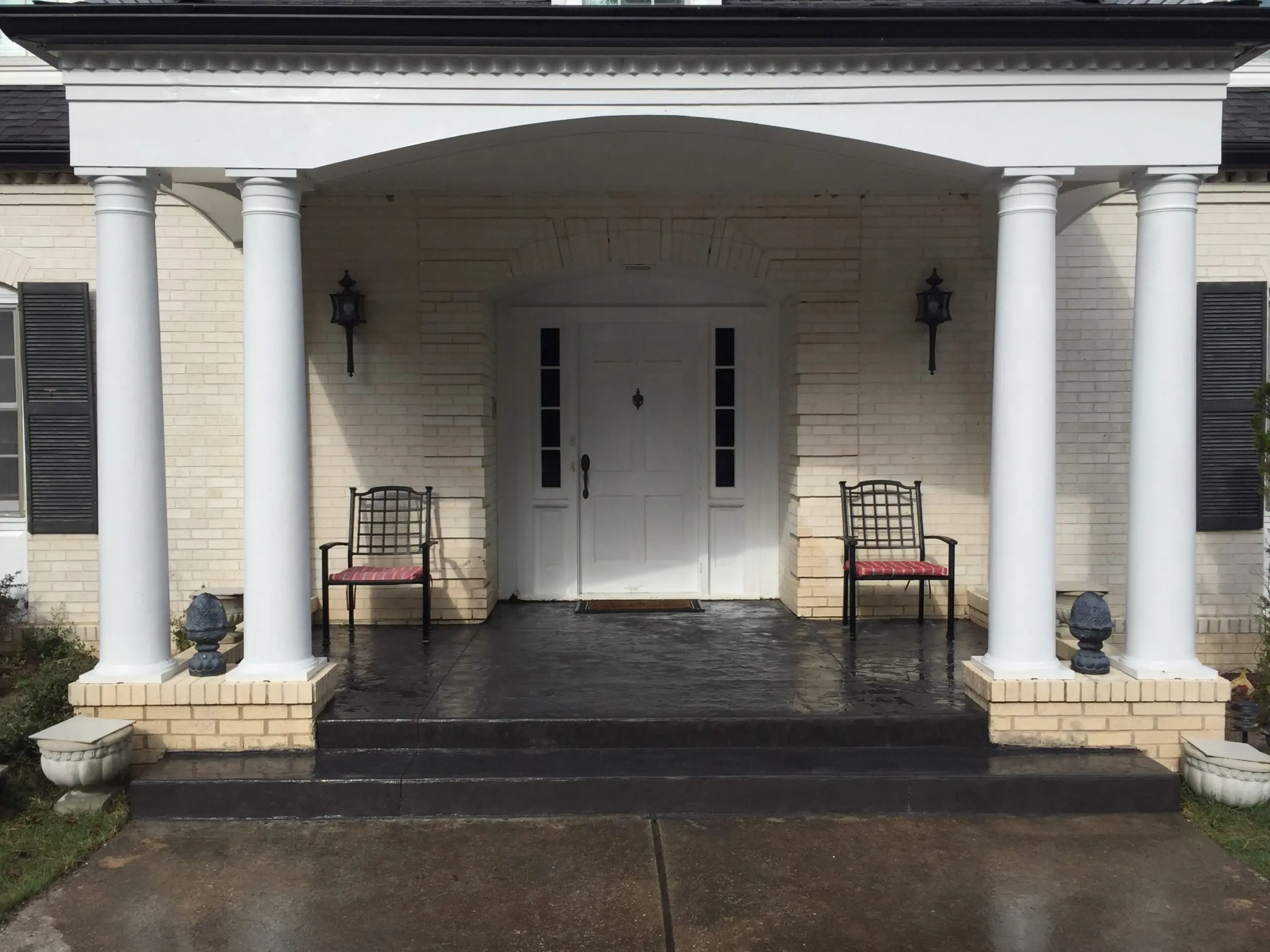 A classic front porch with integral graphite coloring on stamped concrete, flanked by white columns and matching brickwork, creating a striking contrast