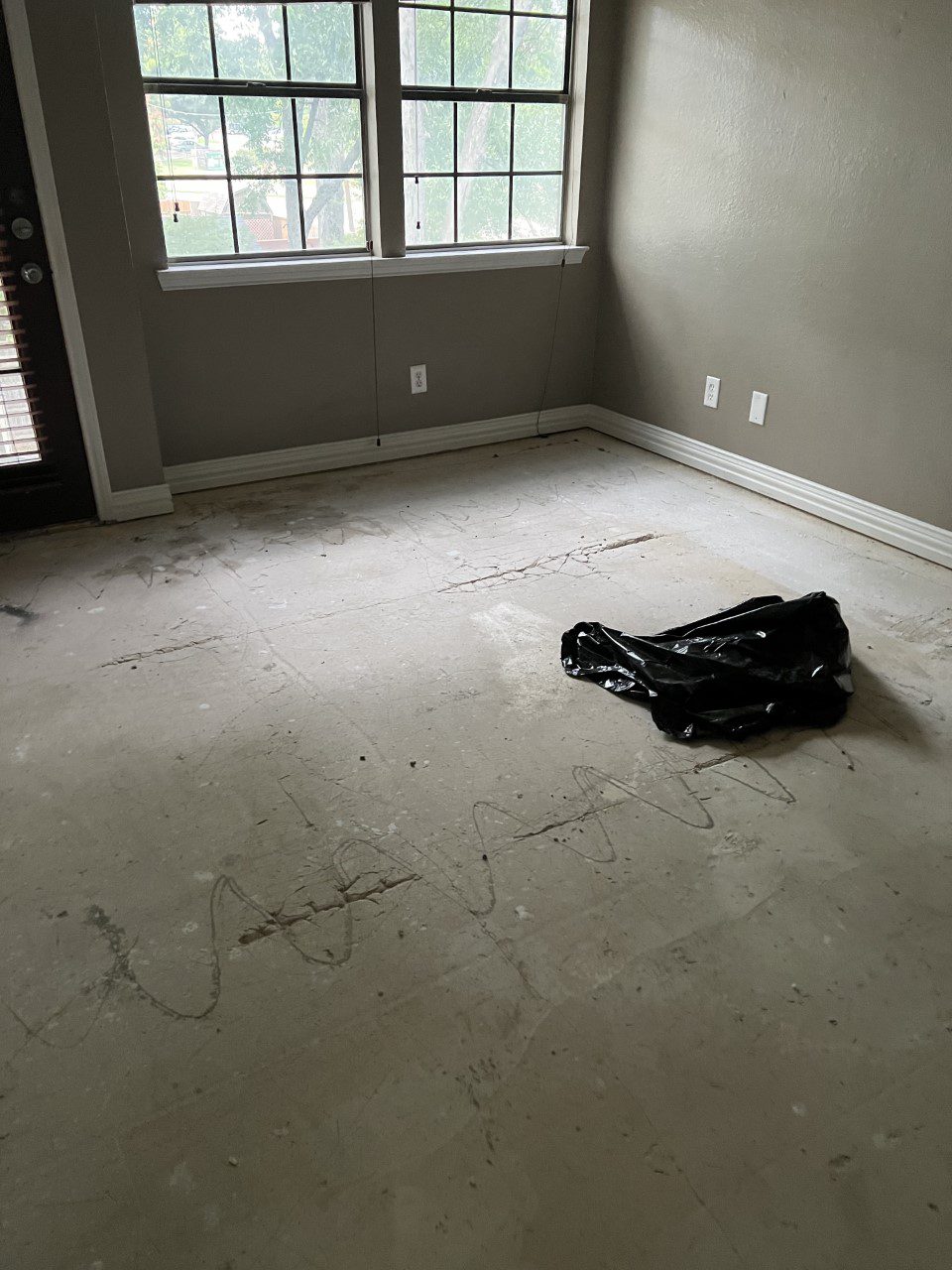 Exposed concrete floor with carpet glue residue and visible cracks after carpet removal, awaiting restoration and transformation.