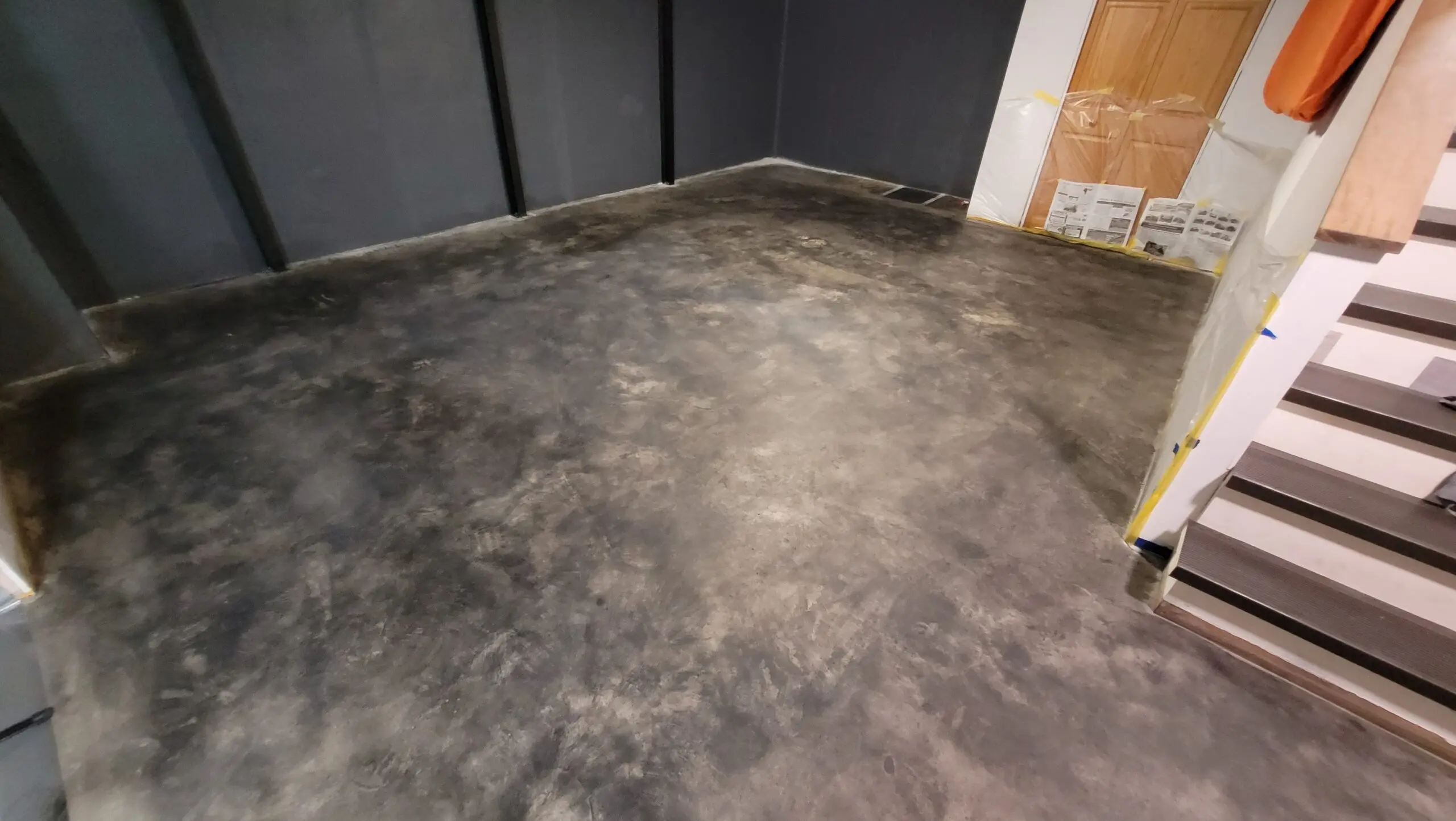 Black stained concrete basement floor during the staining process, with Bissell SpinWave mop swirls, working towards achieving the desired stone-like appearance.