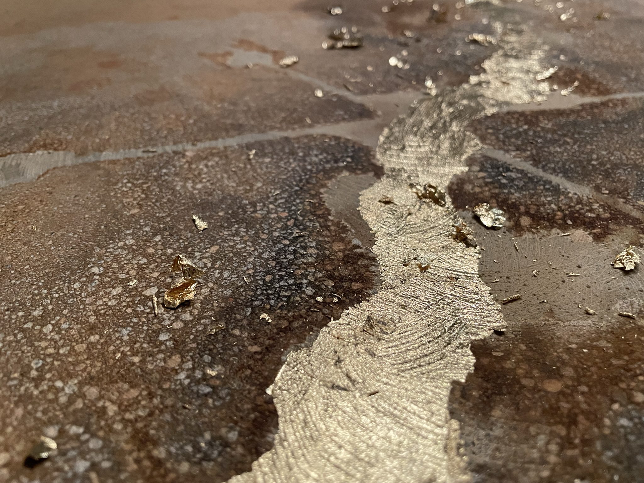 Close-up of a concrete floor with imitation gold leaf applied to a crack after the first coat of sealer