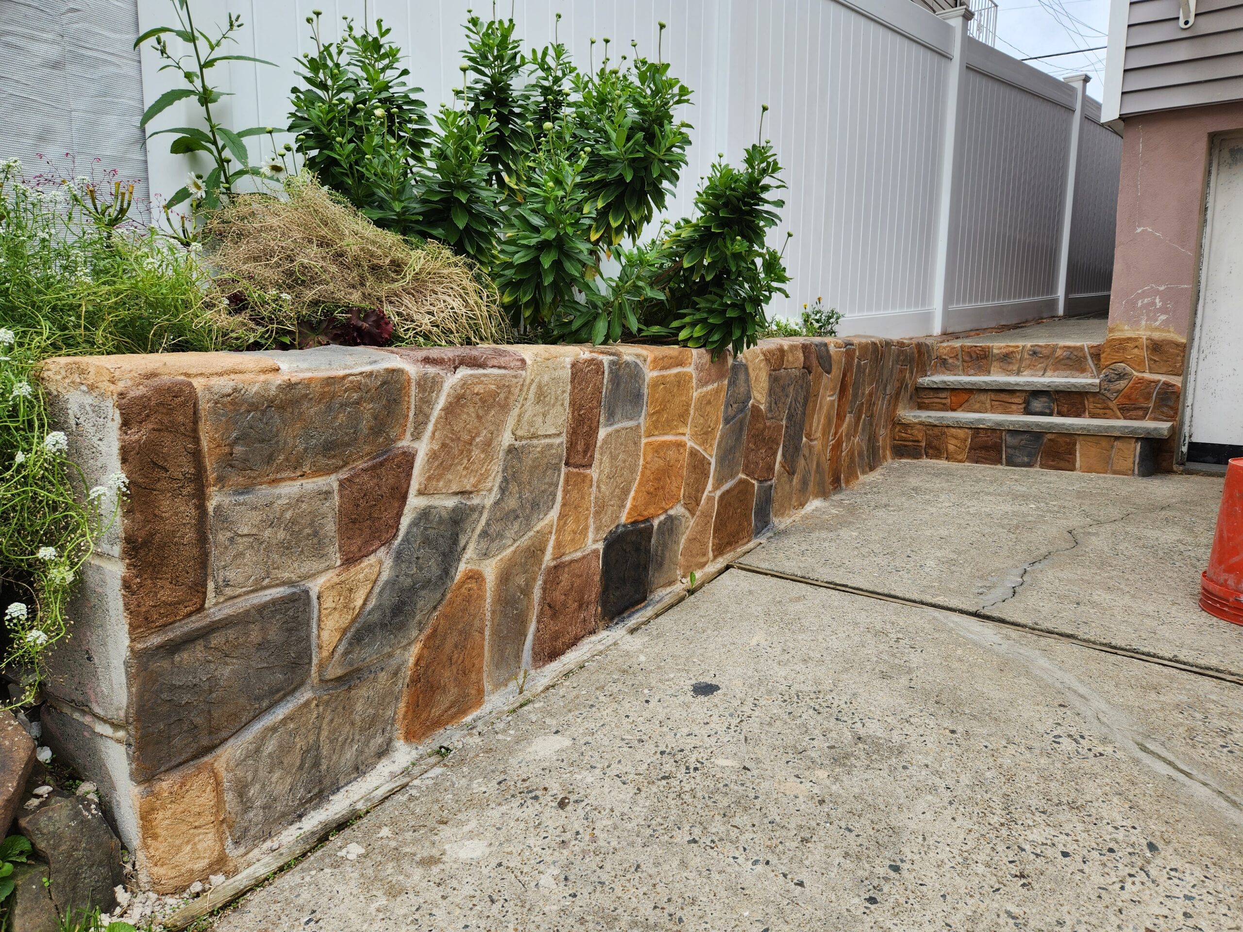 Full view of a faux stone concrete retaining wall in a garden setting