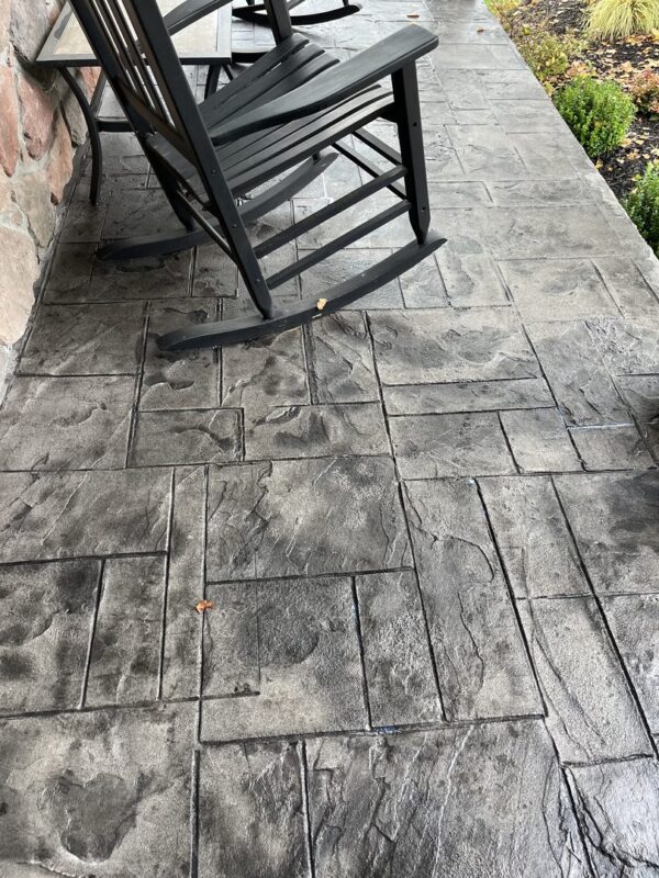 Close-up of a stamped concrete patio stained with ColorWave Steel Gray, featuring a textured surface with rocking chairs on the patio.