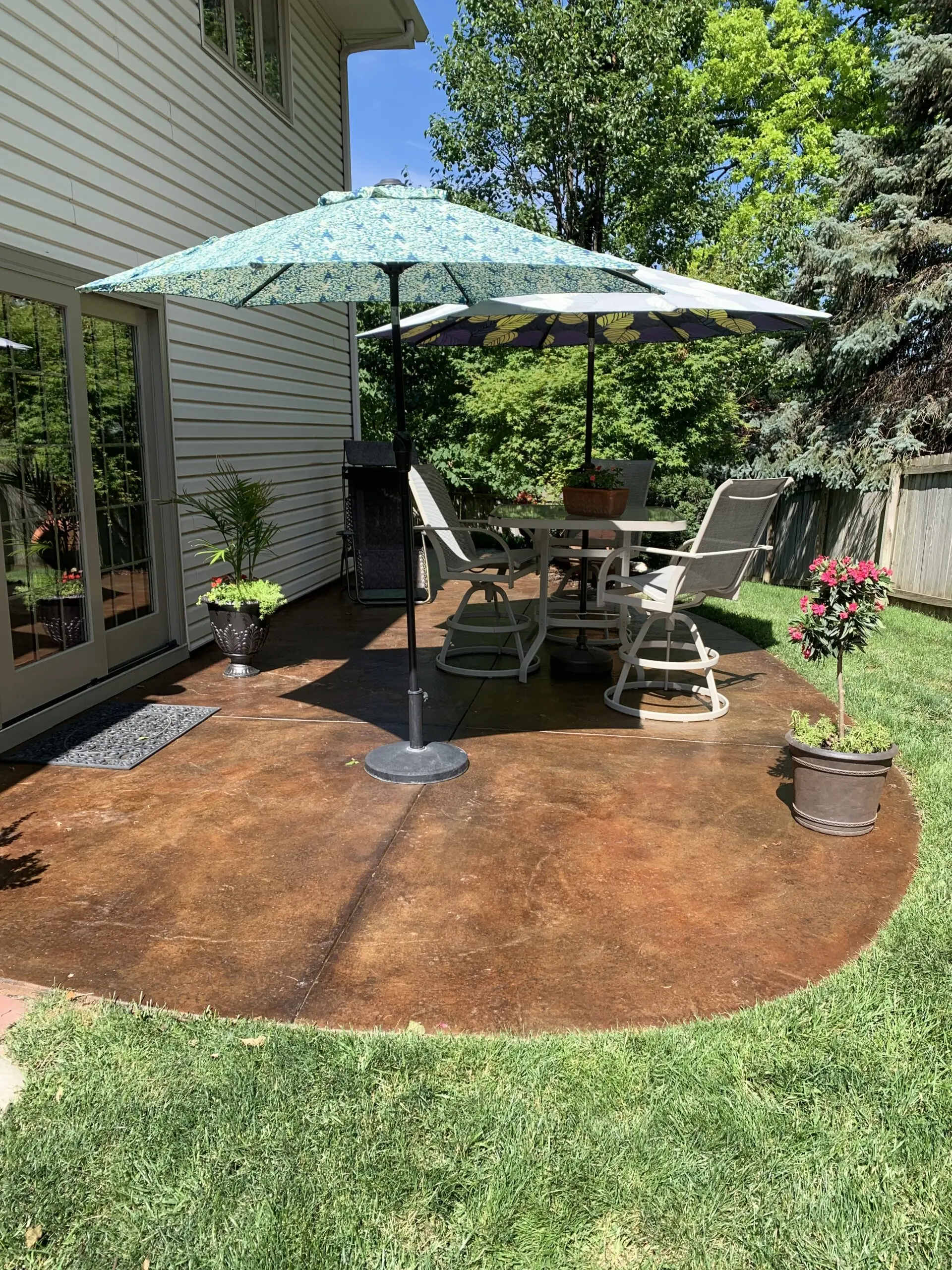 Restored concrete patio stained with Molasses and Mahogany ColorWave, featuring outdoor furniture and umbrellas in a sunny yard.