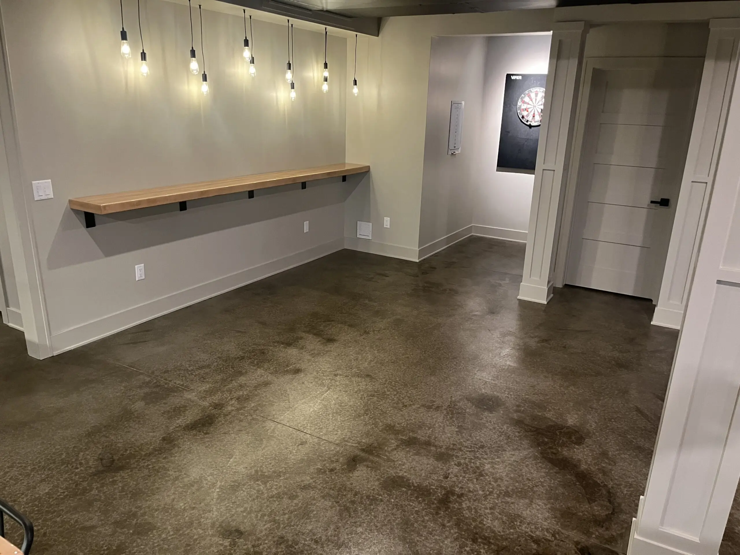 A completed concrete basement floor, stained with Molasses ColorWave, showing a rich, dark brown finish with natural variations and smooth texture across the entire surface.