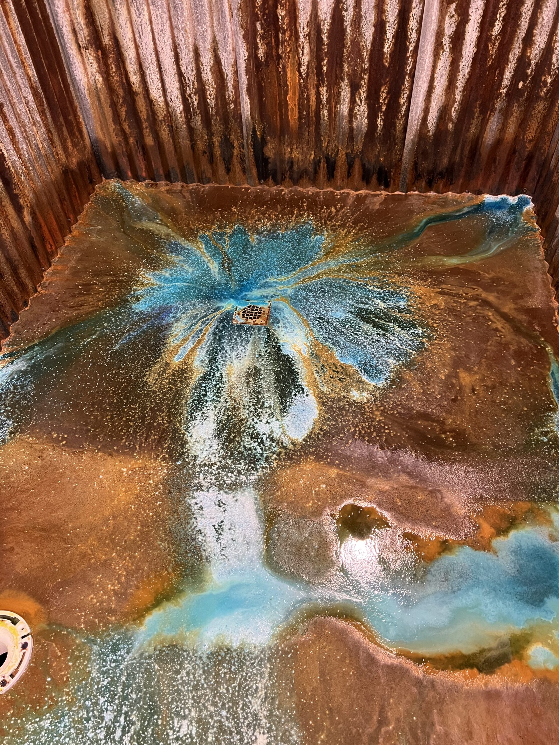 Concrete bathroom floor with an artistic design featuring a central burst of azure blue and white, surrounded by shades of brown and orange, created using Miracle Gro and EverStain acid stain.