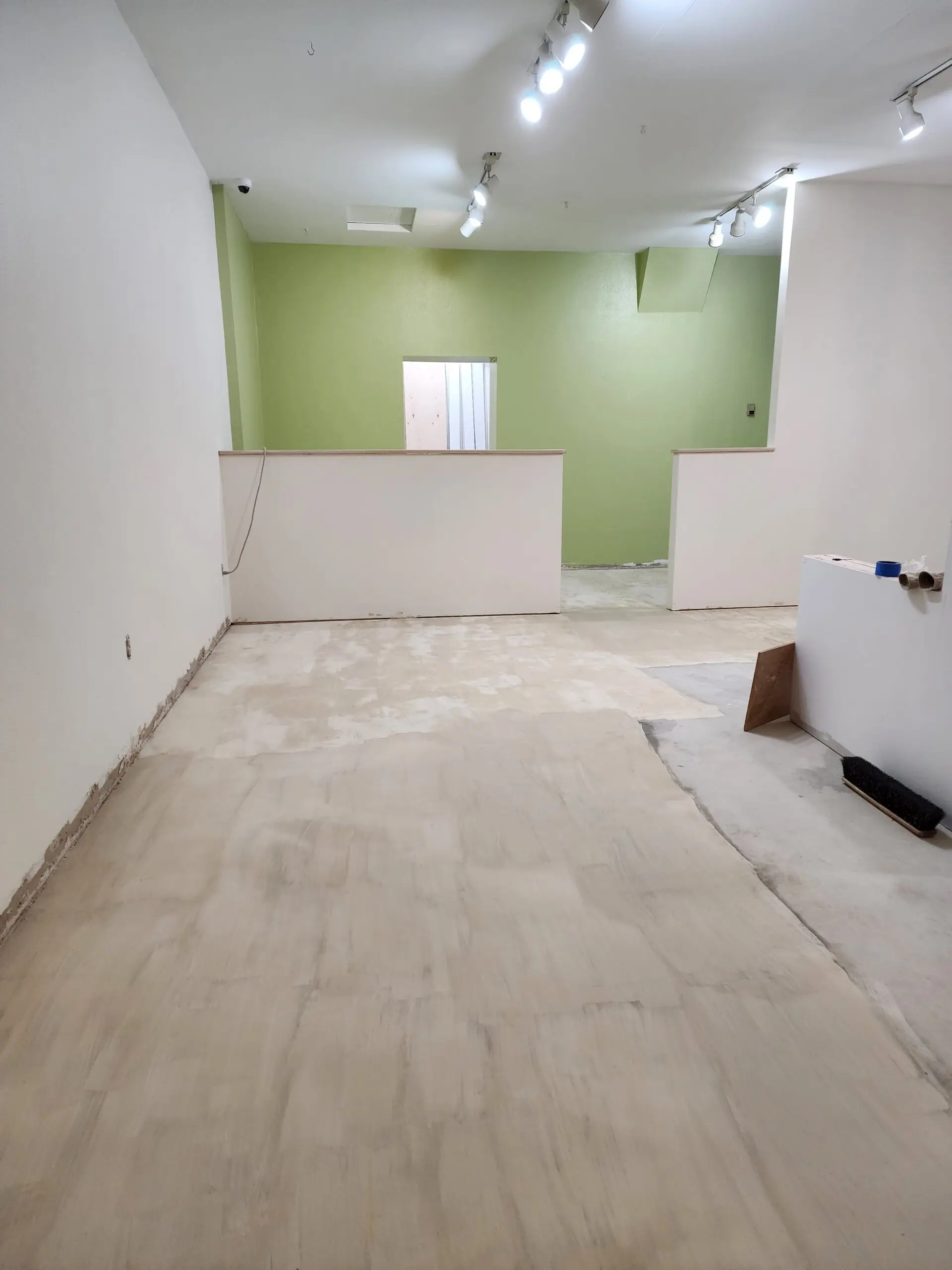 Retail space concrete floor with cream beige pigmented overlay applied using a chip brush
